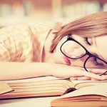 tired student girl with glasses sleeping on books in library